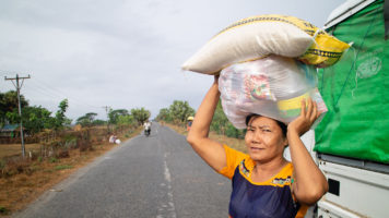 Nainen seisoo kuorma-auton edessä ja kantaa päänsä päällä ruokasäkkejä