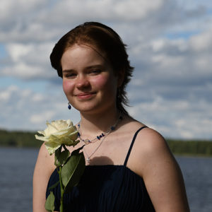 Helena Syyrakki järvimaisema taustallaan, kädessä valkoinen ruusu
