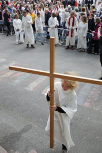 Albaan pukeunut pieni poika kantaa ristiä.