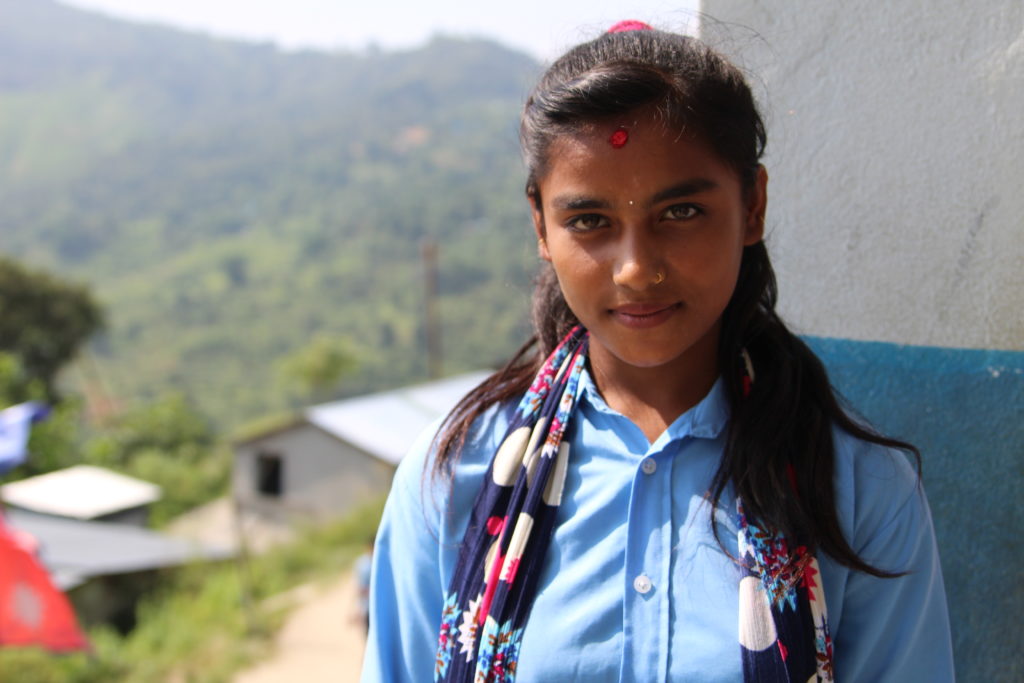7. luokkalainen Manisha hymyilee kameralle koulunsa edessä.