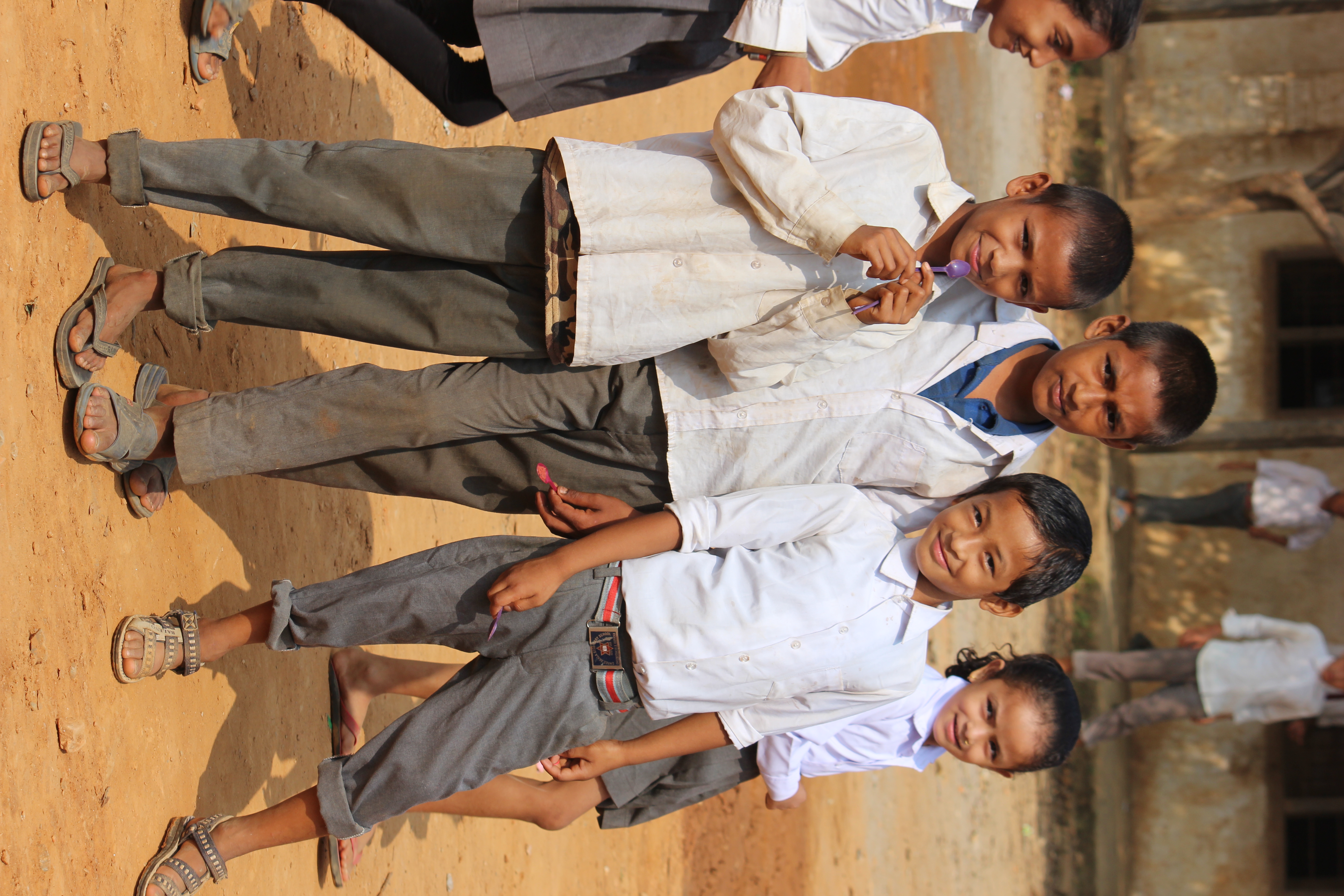 Nepalilaisia koululaisia hymyilee kameralle pölyisissä koulupuvuissa.