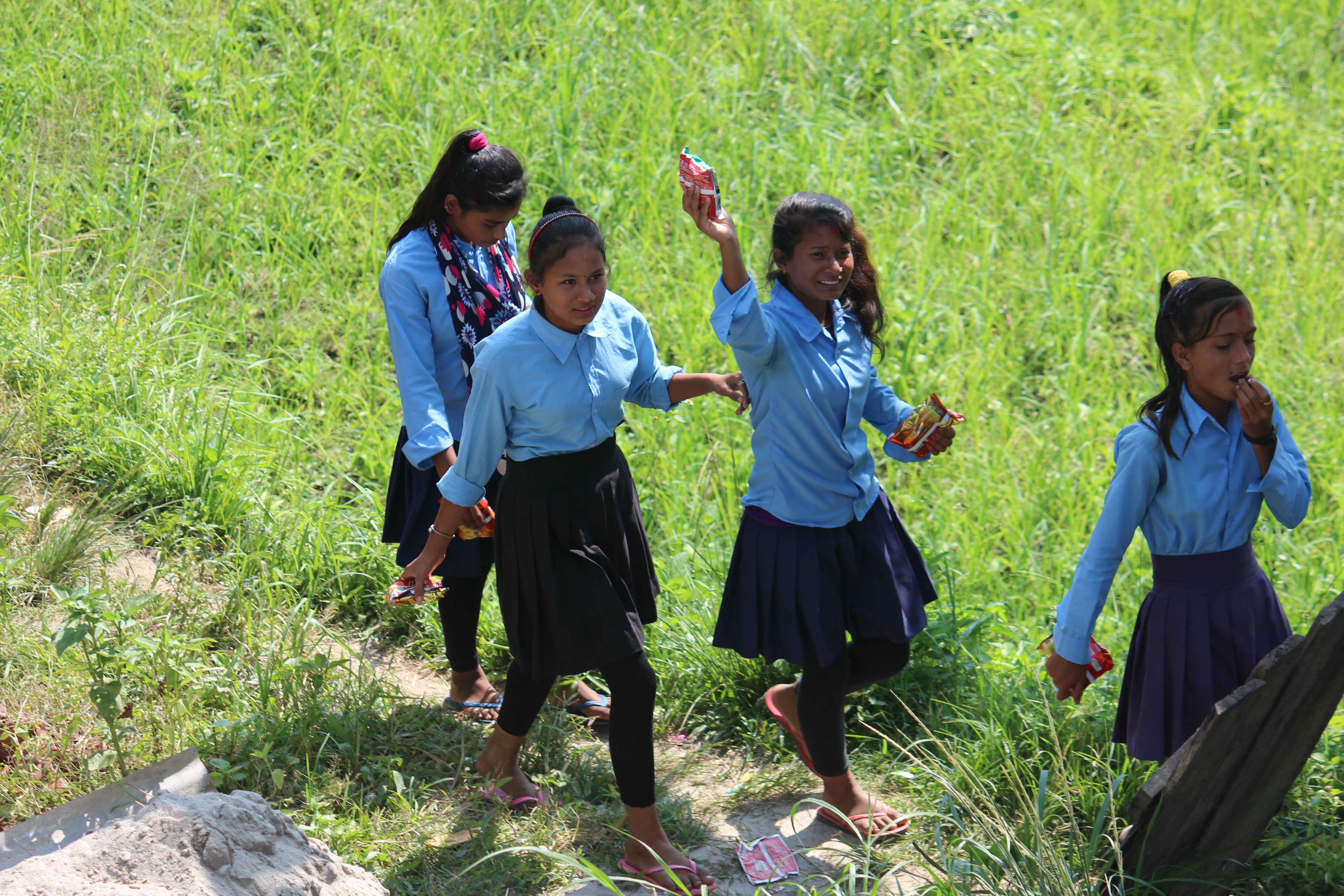 Nepalilaisia oppilaita kävelee pellon poikki hymyillen kouluun.