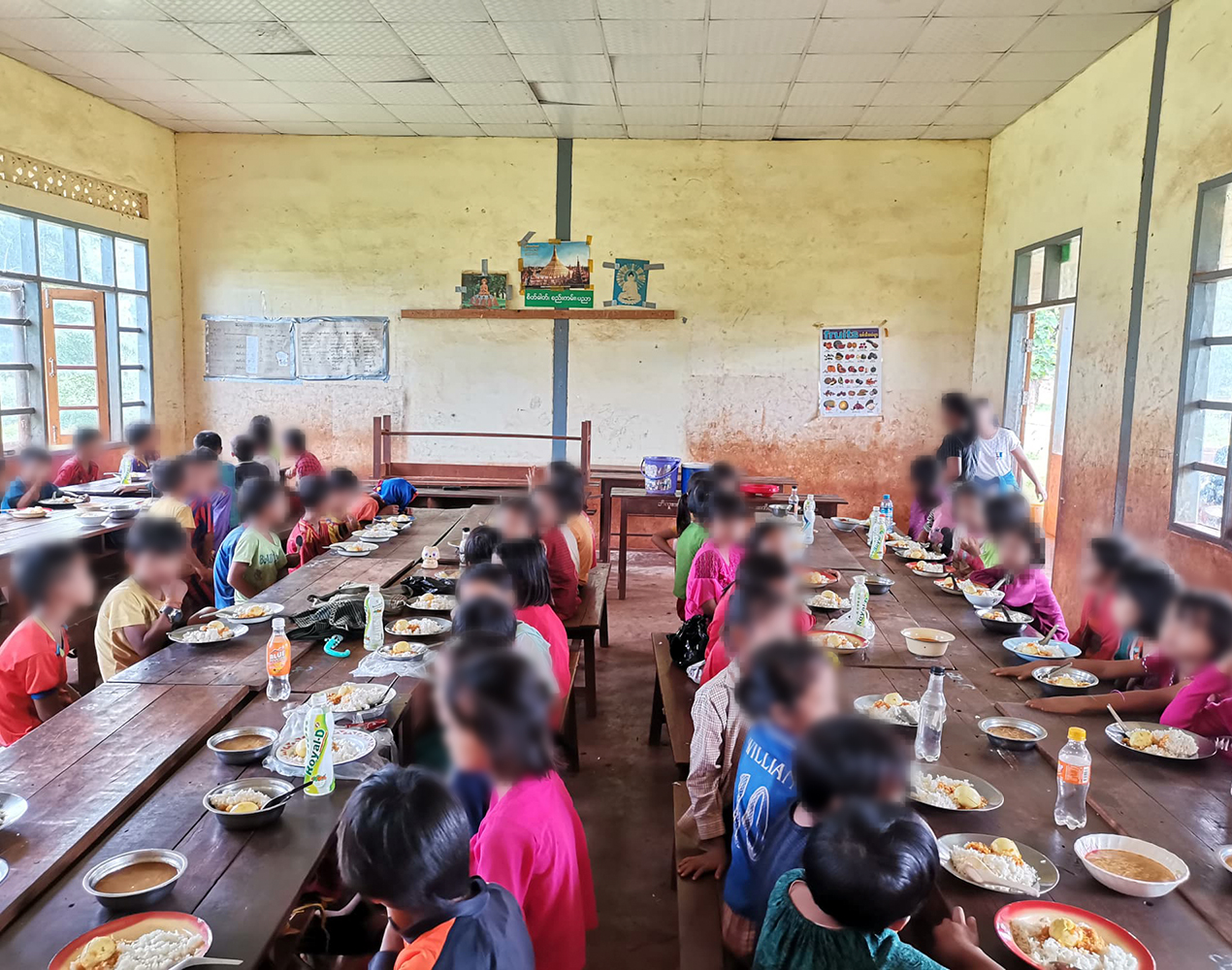 Lapsia pitkien pöytien ääressä syömässä kouluruokaa.