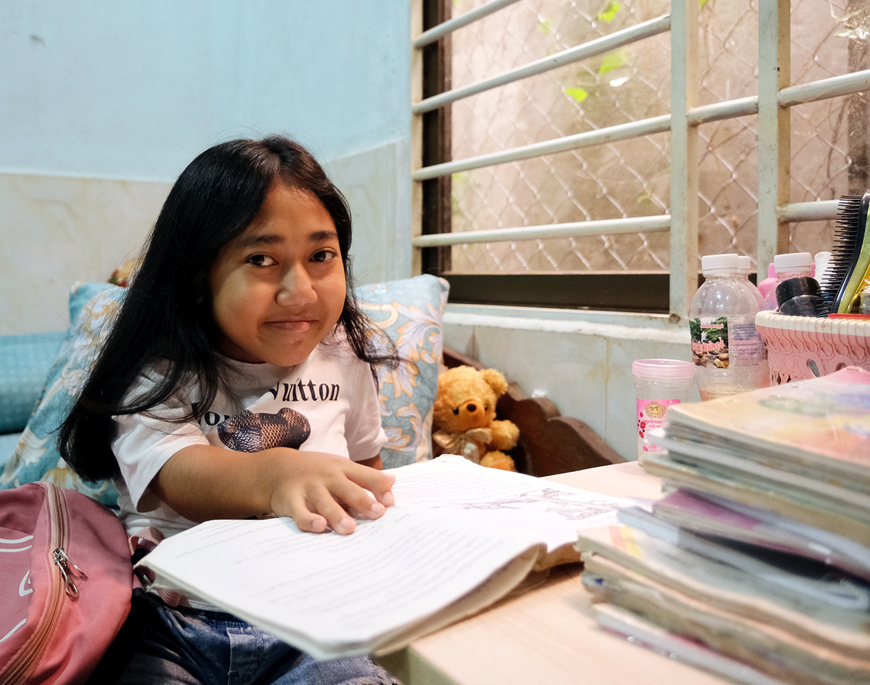 Sok Leap istuu kotona kirjoituspöydän ääressä edessään koulukirja ja hymyilee kameralle.