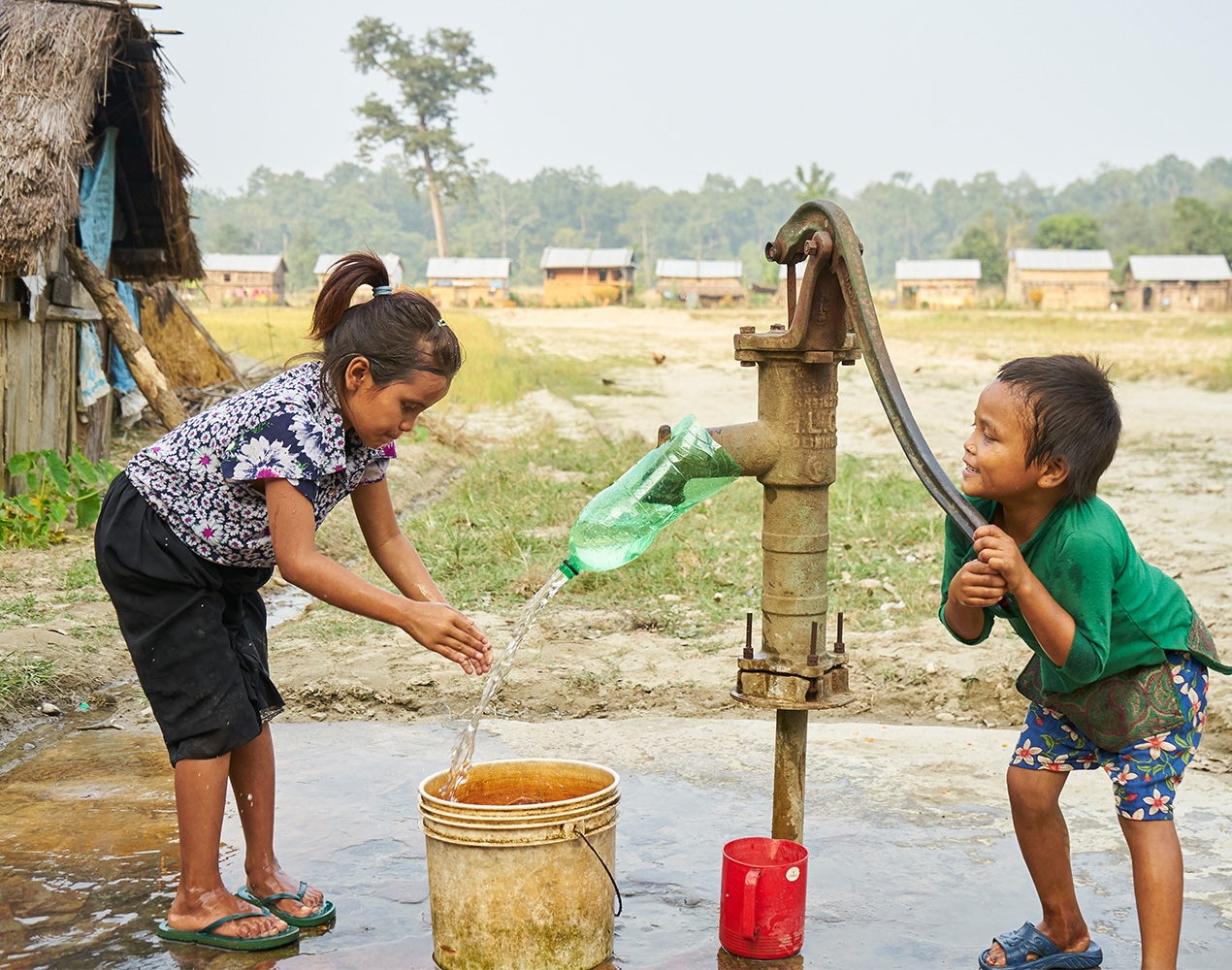 kaksi lasta vesipumpun äärellä pumppaamassa vettä kaivosta