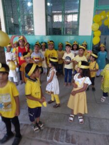 Keltaisiin pukeutuneilla pienillä koululaisilla on myös päässään keltaiset hiuspannat. Ympärillä on keltaisia ilmapalloja.